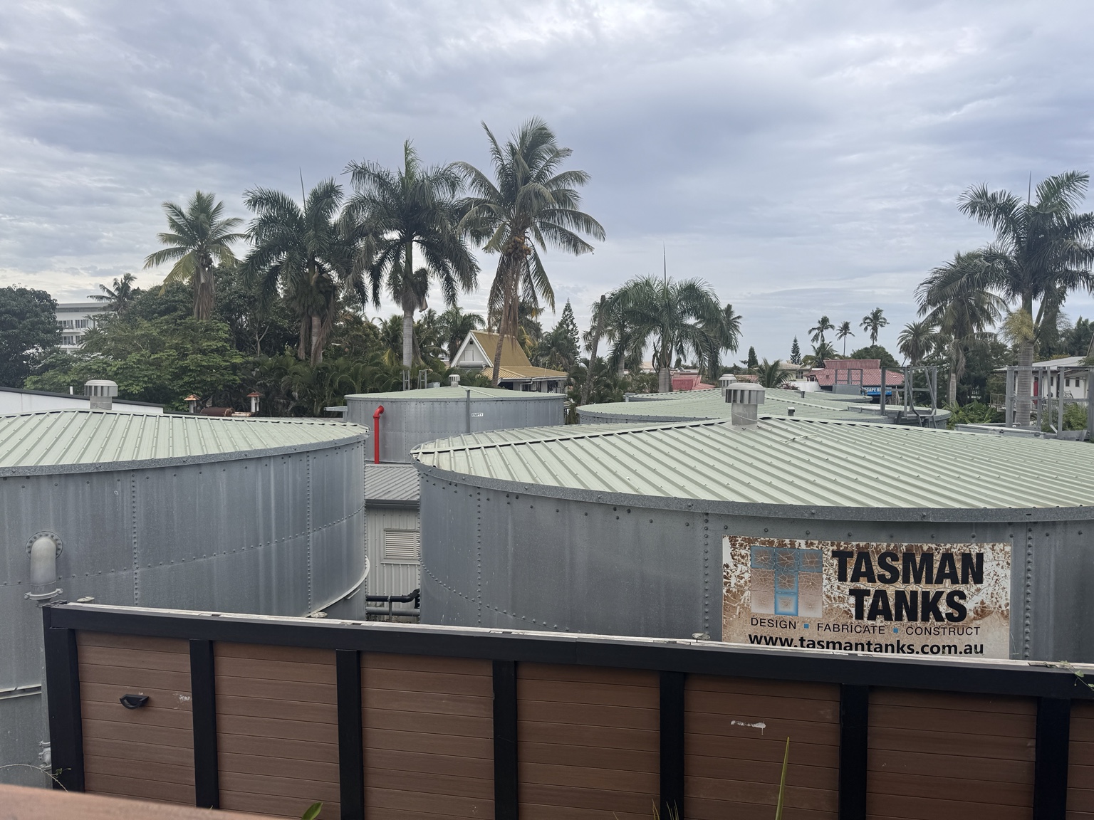 View from the upper-level room walkway across water tanks toward palms and neighboring buildings