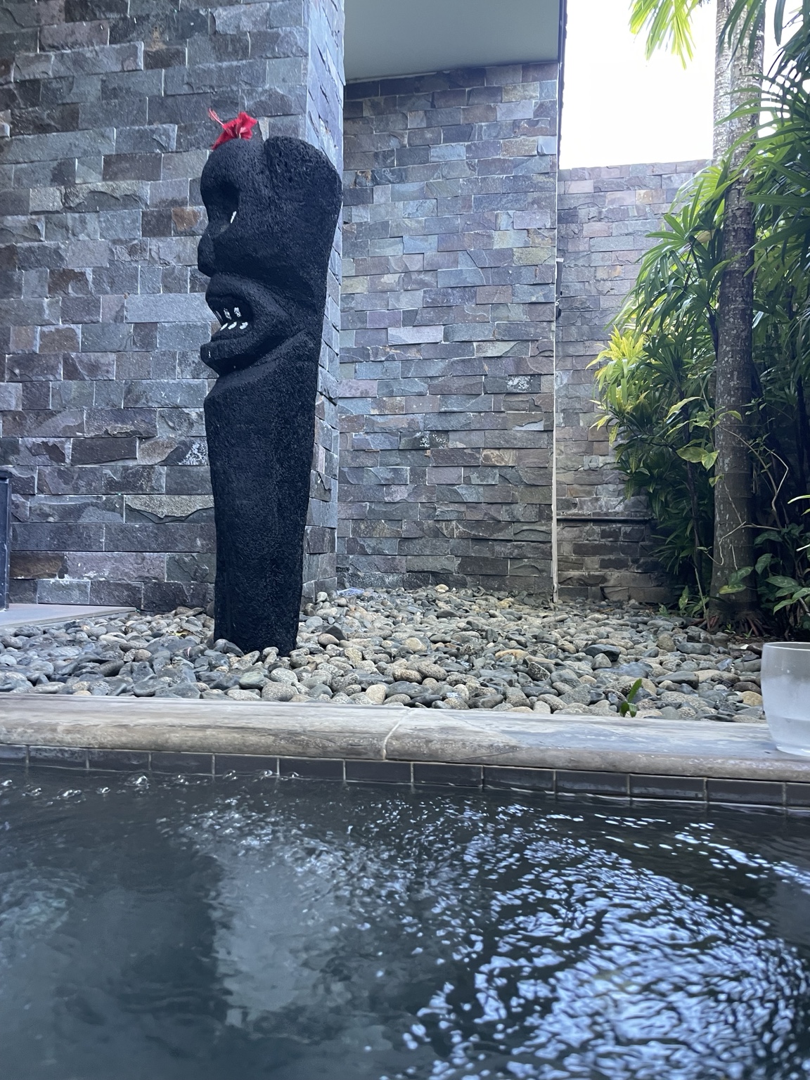 Spa pool beside a sculpture, stone walls and tropical plants